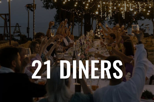21 diner met mensen aan een lange tafel onder sfeerverlichting.