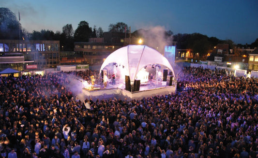 Grote menigte tijdens een festival voor een verlichte witte dome-tent op een plein in de avond.