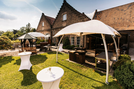 Witte Lounger tenten in een sfeervolle tuinopstelling bij een landhuis, met loungezitjes en statafels tijdens een buitenevent.