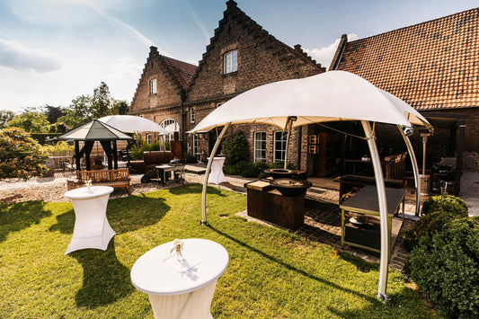 Witte Lounger tenten in een sfeervolle tuinopstelling bij een landhuis, met loungezitjes en statafels tijdens een buitenevent.