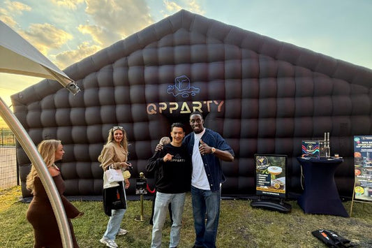 Vier personen voor een grote zwarte opblaasbare feesttent van Qpparty op een buitenevenement