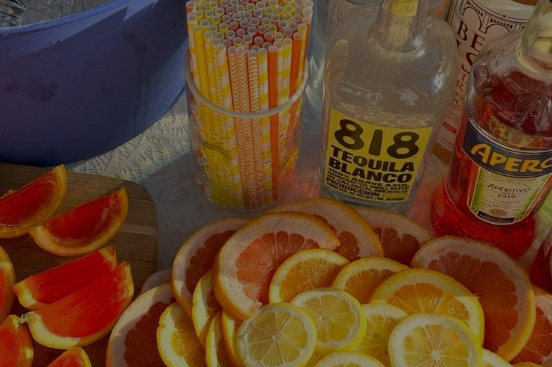 Schijfjes sinaasappel, citroen en limoen naast flessen tequila, Aperol en frisdrank voor het maken van kleurrijke cocktails.