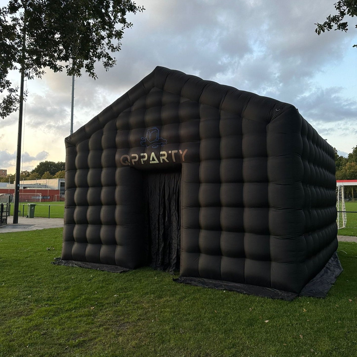 Grote zwarte opblaastent van Qpparty, geplaatst op een grasveld, met afmetingen van 3,5 meter hoog, 5,5 meter lang en 4,8 meter breed. Met een capaciteit van 40 tot 50 man.