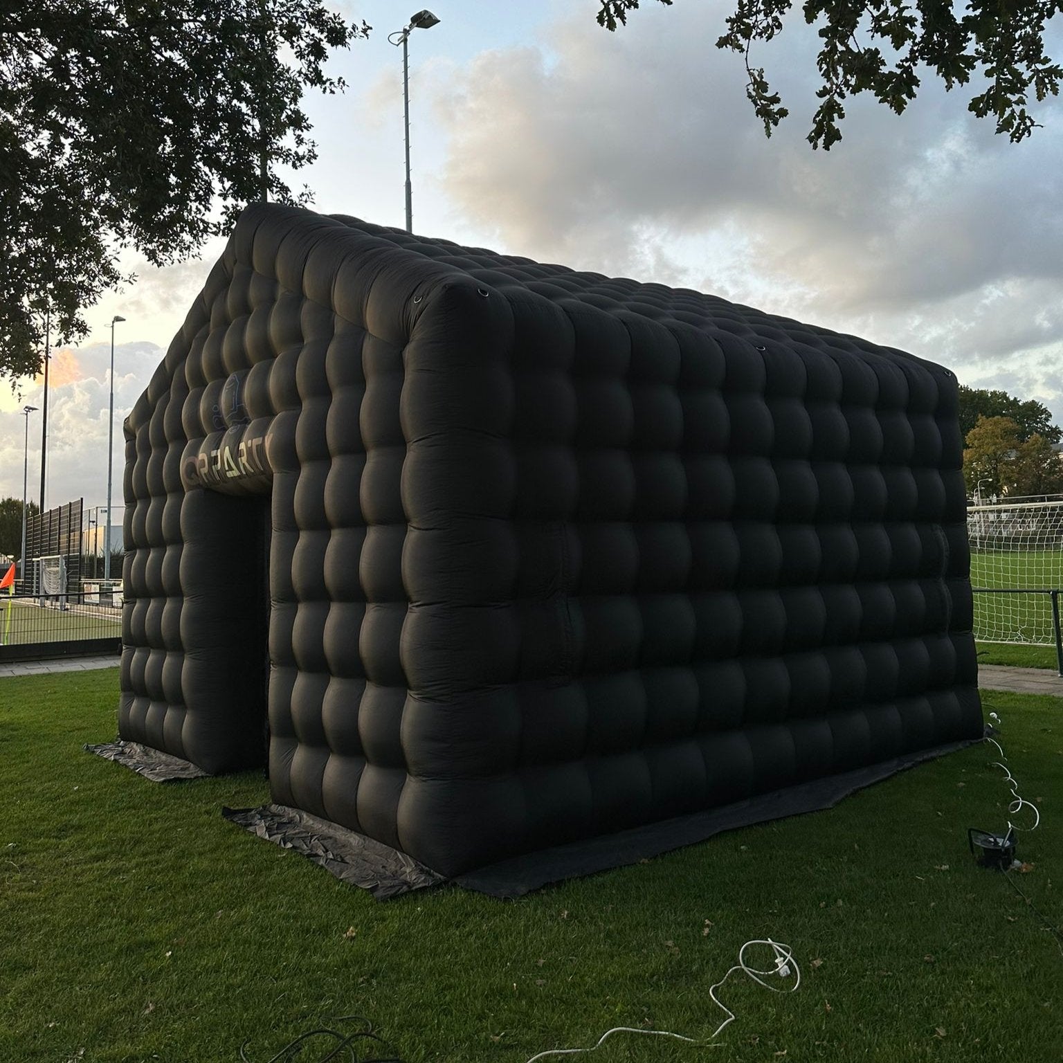 Zijaanzicht van een grote zwarte opblaastent van Qpparty, opgesteld op een grasveld, met afmetingen van 3,5 meter hoog, 5,5 meter lang en 4,8 meter breed. Met een capaciteit van 40 tot 50 man.