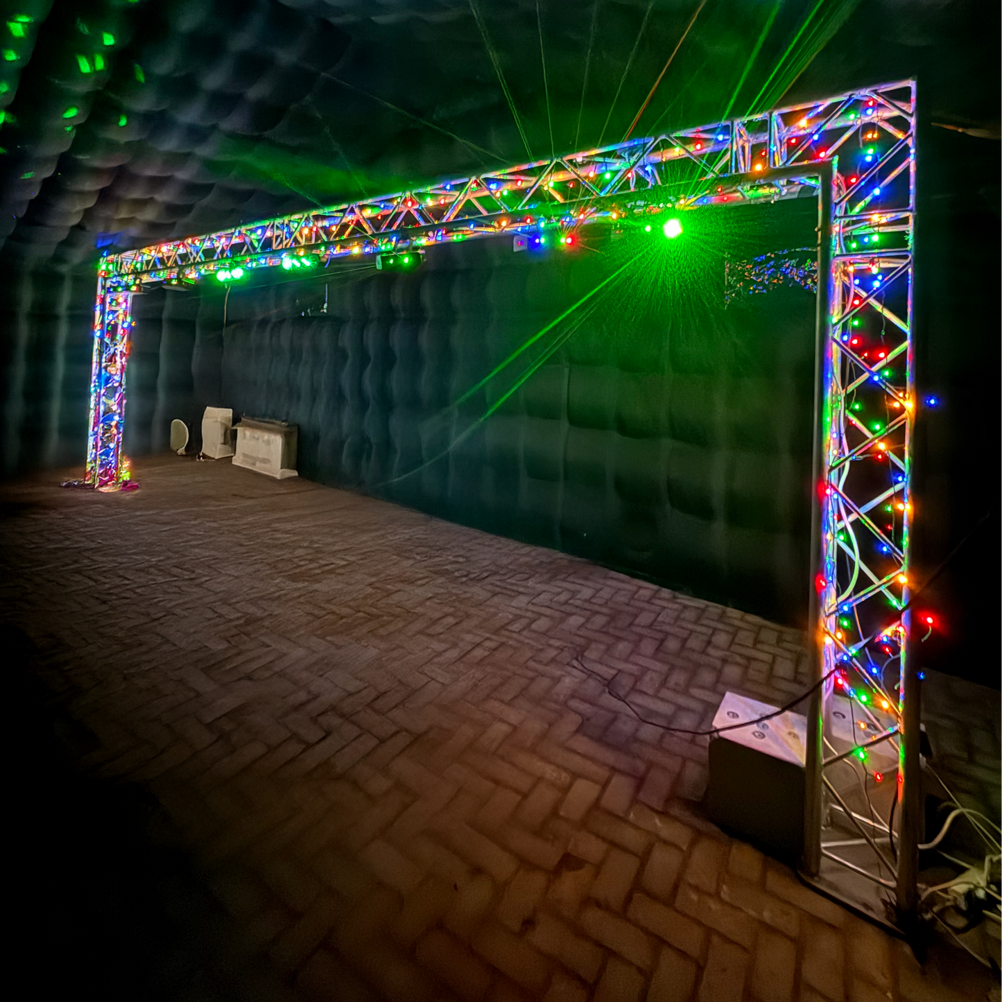 Foto van een verlichte trussboog van QPparty, 2,3 meter hoog en 6,6 meter breed, uitgerust met felgekleurde LED-verlichting en geplaatst in een donkere indoorruimte.