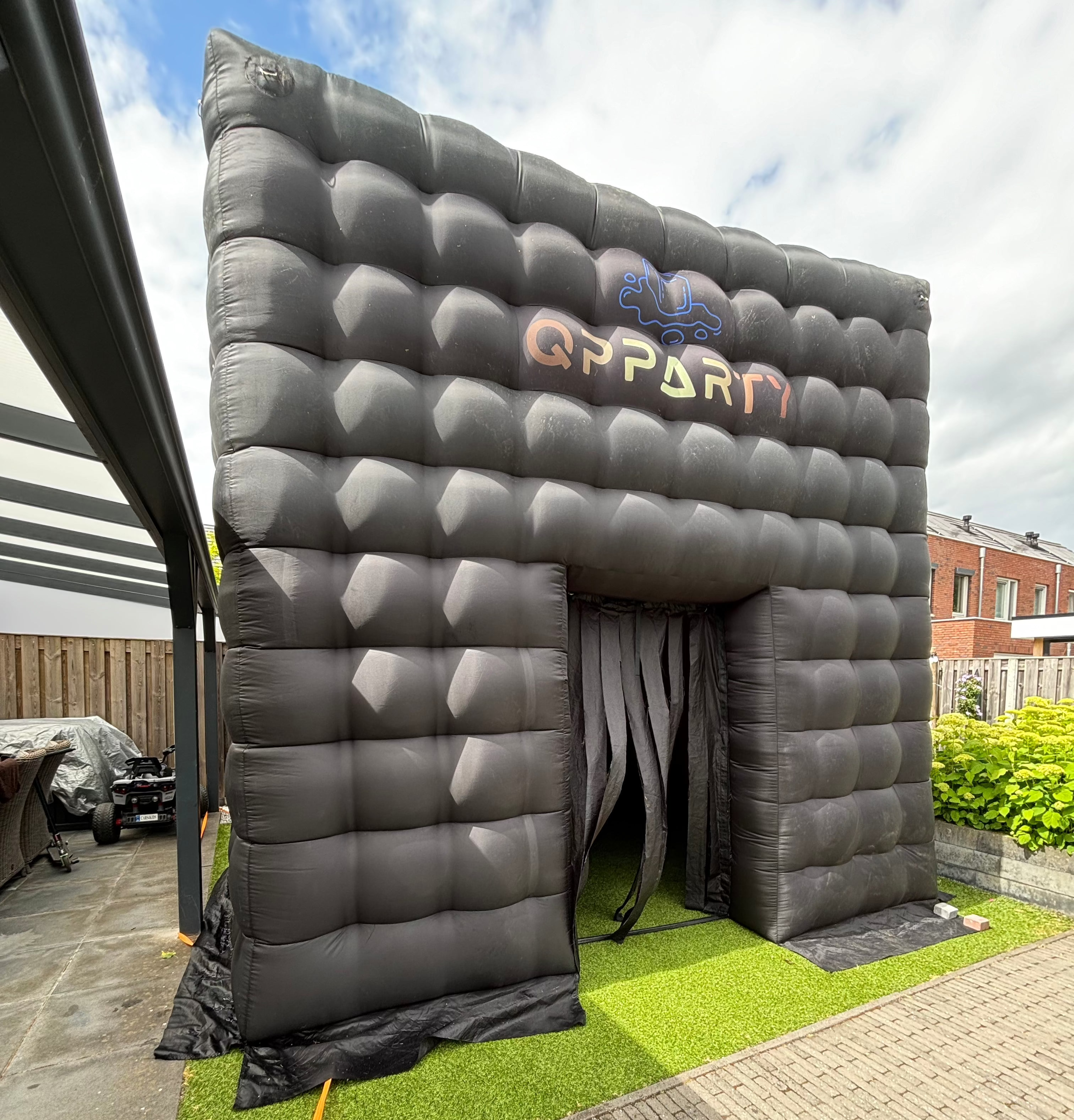 Zwarte opblaasbare tent, geplaatst op kunstgras in een tuinomgeving. Met een capaciteit van 30 tot 40 gasten.