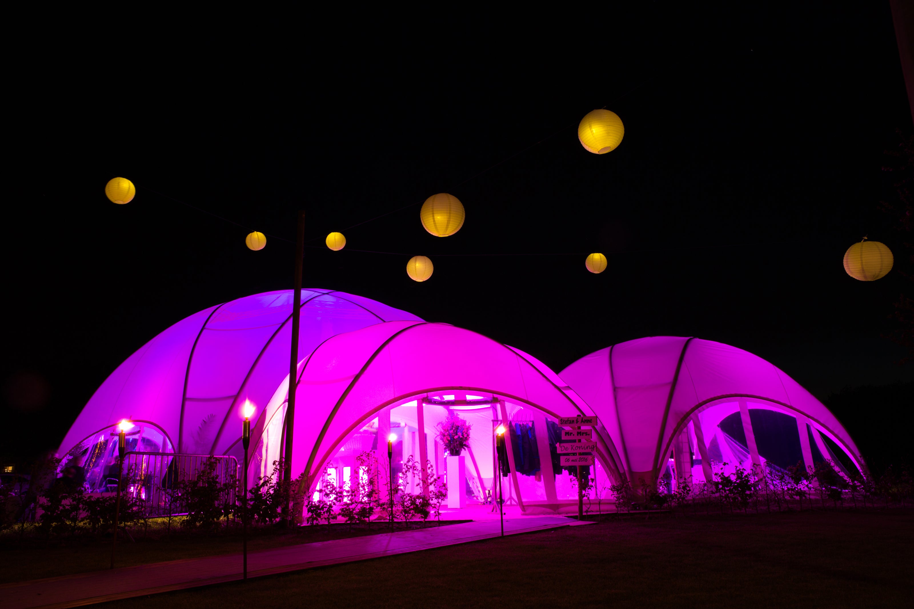 Hexadome M trouwtent met sfeervolle roze verlichting tijdens een avondbruiloft in dorpsstijl.