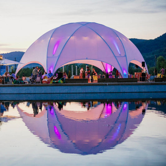 Hexadome L eventtent bij strand- en zwembadterras, sfeervol verlicht voor een outdoor evenement aan het water.