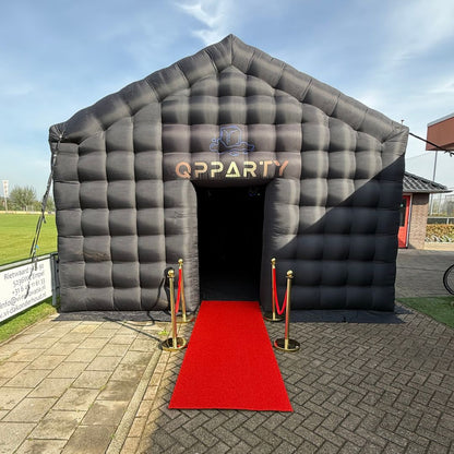 Zwarte opblaasbare feesttent van Qpparty met een rode loper en gouden afzetpaaltjes bij de ingang.