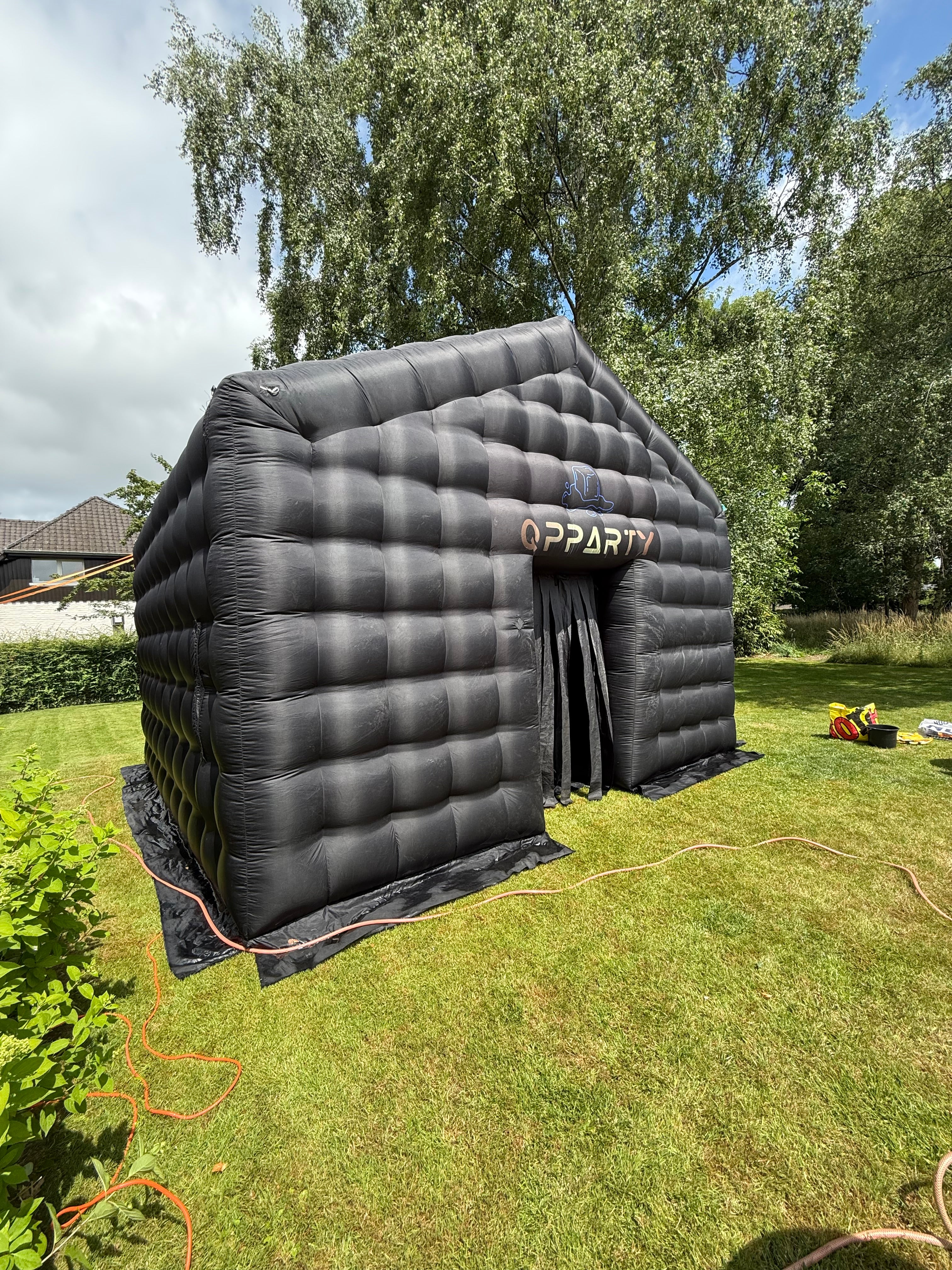 Grote zwarte opblaasbare tent van Qpparty opgesteld op een grasveld